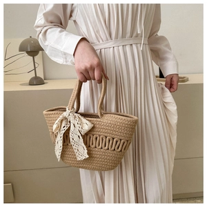 Detail of hand-woven straw tote with wavy texture and cream lace bow accessory