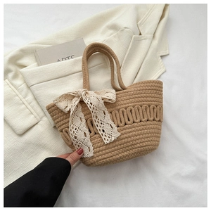 Detail of light brown woven tote bag featuring a white lace bow and wavy knit texture
