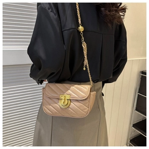 Detail of beige quilted mini crossbody bag with gold chain strap worn by a model