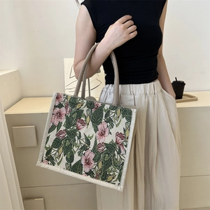 Floral knit tote bag with pink flowers and green leaves in a stylish handheld display