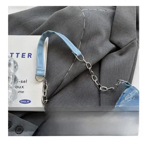 Detail of blue denim shoulder bag with silver metal chain strap on fabric background