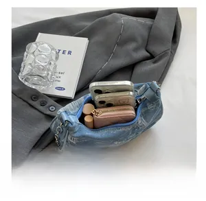 Detailed view of spacious denim underarm bag holding two phones, wallet and lipsticks