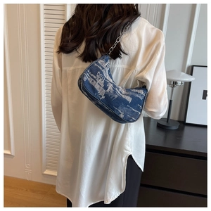 Detailed view of a blue denim baguette bag with silver chain strap on a model's shoulder