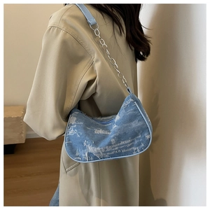 Blue denim hobo bag with silver chain strap worn by a model in a minimal interior