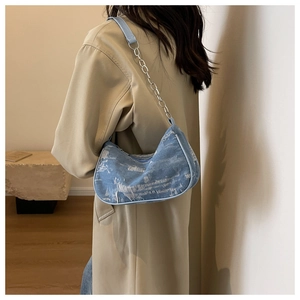 Détail du sac sous le bras en denim bleu clair avec tissu usé et bandoulière chaîne