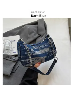 Detail of dark blue denim underarm bag with distressed texture and silver chain strap