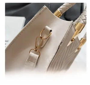Detail showing woven leather handle and light gold hardware hooks of the cream handbag