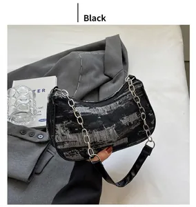 Close-up of distressed black denim baguette bag with silver chain and leather strap