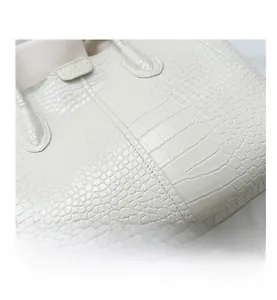 Macro view of white faux crocodile leather texture and reinforced stitching on a tote bag