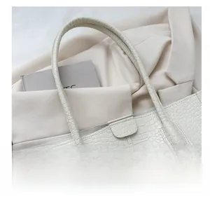 Detail of white crocodile embossed tote bag showing reinforced shoulder strap attachment