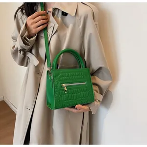 Detail of green crocodile embossed handbag with silver zipper and round handle