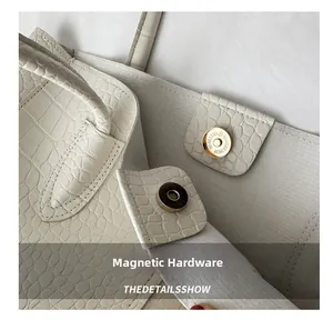 Close-up of golden magnetic snap and crocodile pattern on white leather tote bag