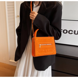 Detail of orange quilted tote with crocodile texture and iconic zipper front pocket