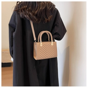 Detailed view of khaki quilted crossbody bag with woven handle on a black coat