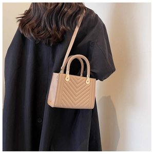 Chic beige V-quilted crossbody bag with woven handle shown on a black winter coat