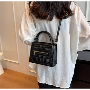 Detailed view of black crocodile pattern crossbody bag with golden zipper and handle