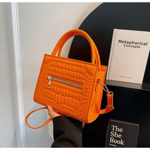 Detail of orange tote bag showing crocodile pattern texture and golden hardware