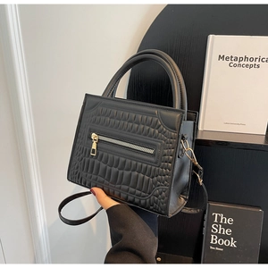 Detail of black crocodile texture handbag featuring golden zipper and slim shoulder strap