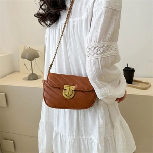 Caramel crossbody chain bag with quilted pattern and gold circular buckle on white dress