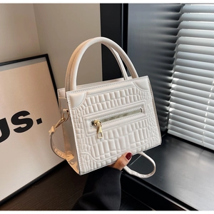 Detail of white crocodile embossed square handbag with golden zipper and top handle