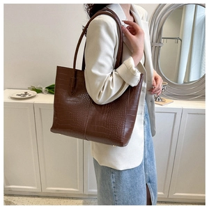 Detail of dark brown croc-embossed tote bag with golden protective feet and premium texture