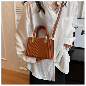 Detail of brown faux leather handbag with V-shaped quilting and woven handle accents