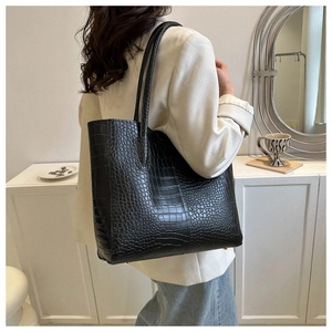 Detailed view of black crocodile pattern tote bag with gold metal studs shown in lifestyle setting