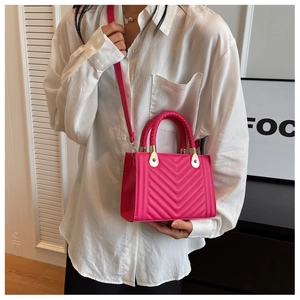 Detail of rose red crossbody bag with V-shaped quilting and gold hardware on model