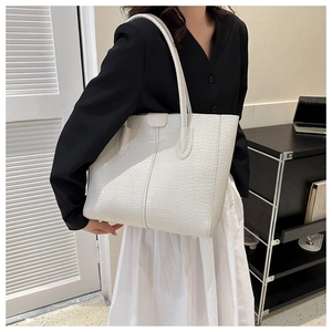 Detail of white crocodile embossed tote bag featuring high-quality leather texture and studs