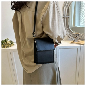 Detail of a black faux leather rectangular crossbody bag with a sleek golden metal clasp