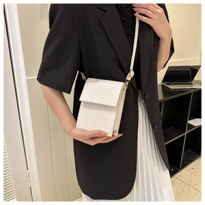 Detail view of a white minimalist PU leather crossbody bag worn with a chic outfit