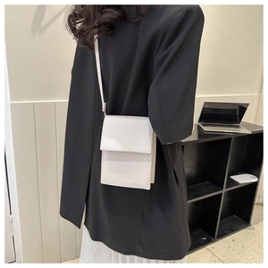 Detailed view of a white rectangular flap crossbody bag worn with a black blazer suit