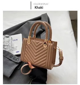 Close-up of khaki V-quilted handbag with woven handle and gold hardware on a desk