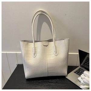 Detail of off-white tote bag featuring crocodile embossed texture and dual straps on a desk