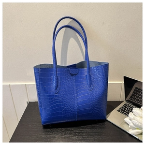 Detail of blue crocodile pattern tote bag with dual straps on an office desk