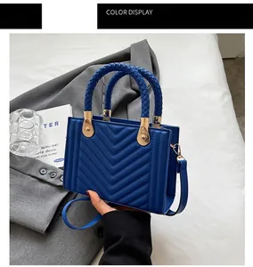 Detail of blue leather handbag with V-quilted pattern and woven handle on grey blazer