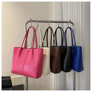 Five crocodile pattern tote bags in various colors hanging on a display rack