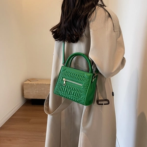 Green faux-crocodile tote bag with metal zipper and adjustable strap shown on beige coat