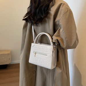 White croc-effect crossbody bag with circular handles shown on a model in a trench coat