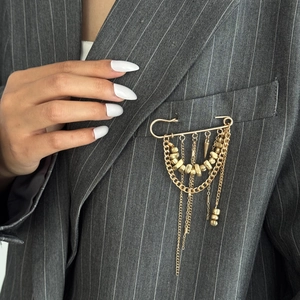 Close-up of golden layered chain brooch with metallic beads on a grey striped suit