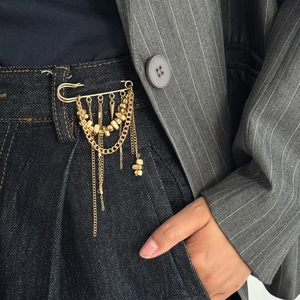 Detail of gold fringe brooch with metal beads styled as a decorative chain on denim jeans