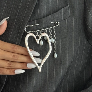 Detail of a silver heart pin with baroque pearls and fringe on a pinstripe blazer