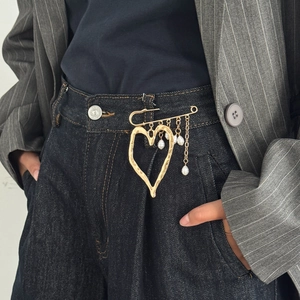 Detailed view of a gold hollow heart brooch with pearl chains on denim fabric