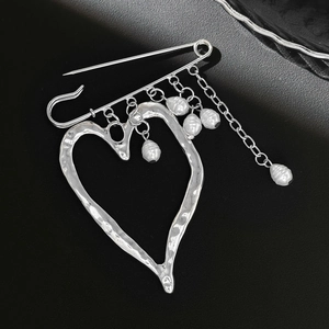 Macro detail of large silver heart pin brooch with hammered texture and dangling pearls