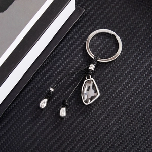 Detail of silver keyring with black braided rope and grey crystal charm on textured surface