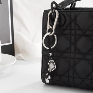 Detail of silver heart keychain with grey crystals on a black quilted leather handbag