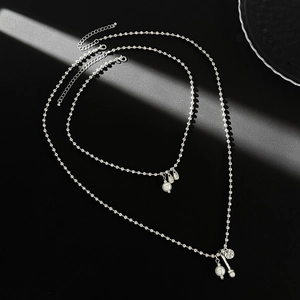 Détail macro du collier à billes argentées avec perles et pendentif pièce en métal