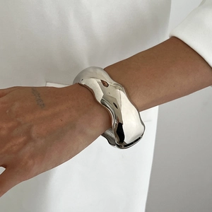 Detailed macro shot of a wide liquid metal irregular wavy silver cuff bracelet on wrist