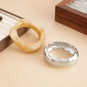 Detail view of irregular marble resin bangle and wavy silver metal bracelet on wood tray