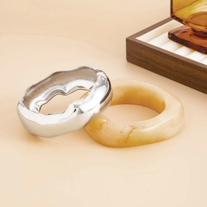 Detail of silver wavy metal bracelet and amber resin bangle on minimalist beige background